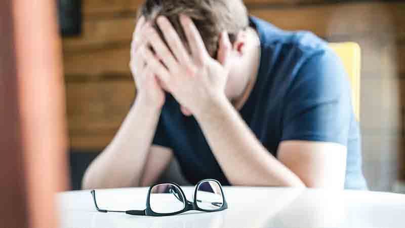 A man at a table with his head in his hands, his glasses set aside